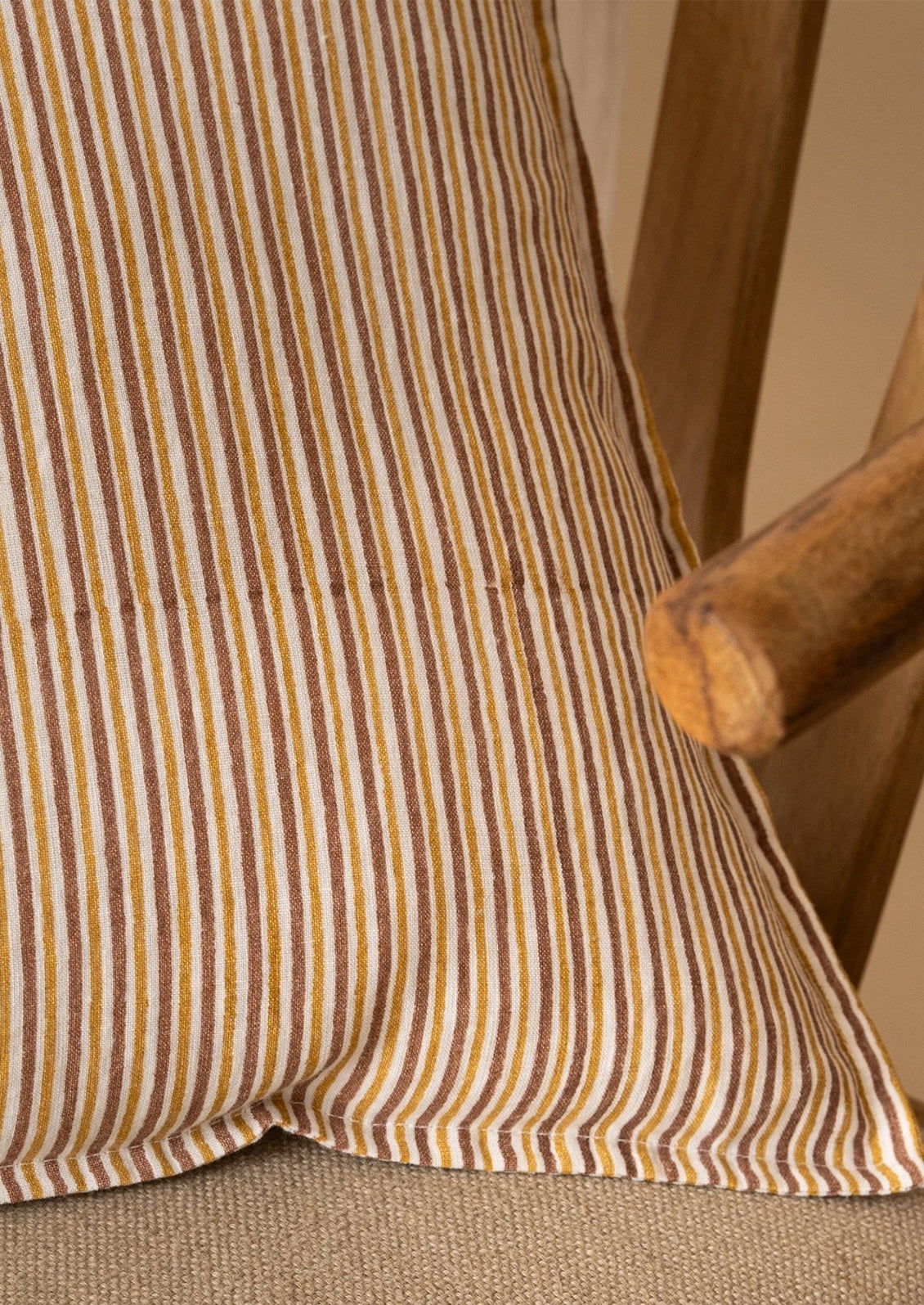 Close-up of a striped fabric cushion or pillow in warm brown, tan, and cream tones, resting against a wooden chair.