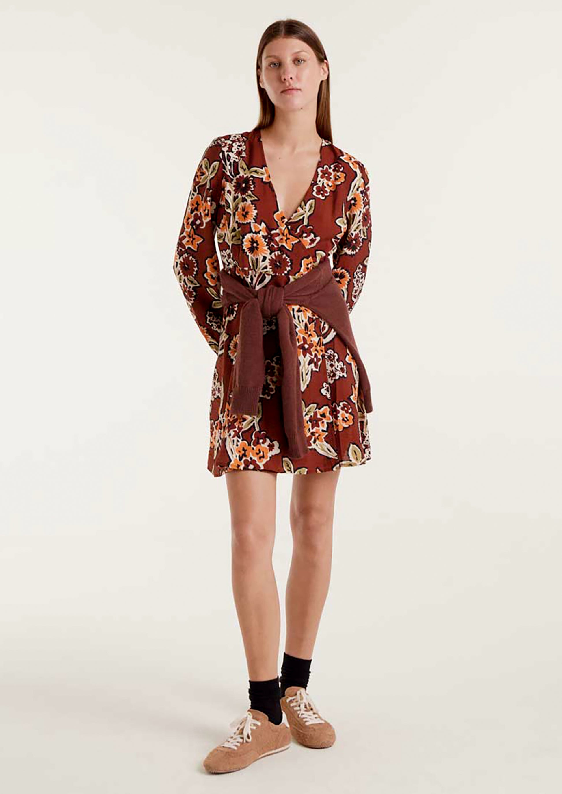 A woman wearing a brown mini long sleeve dress with orange and green floral pattern.