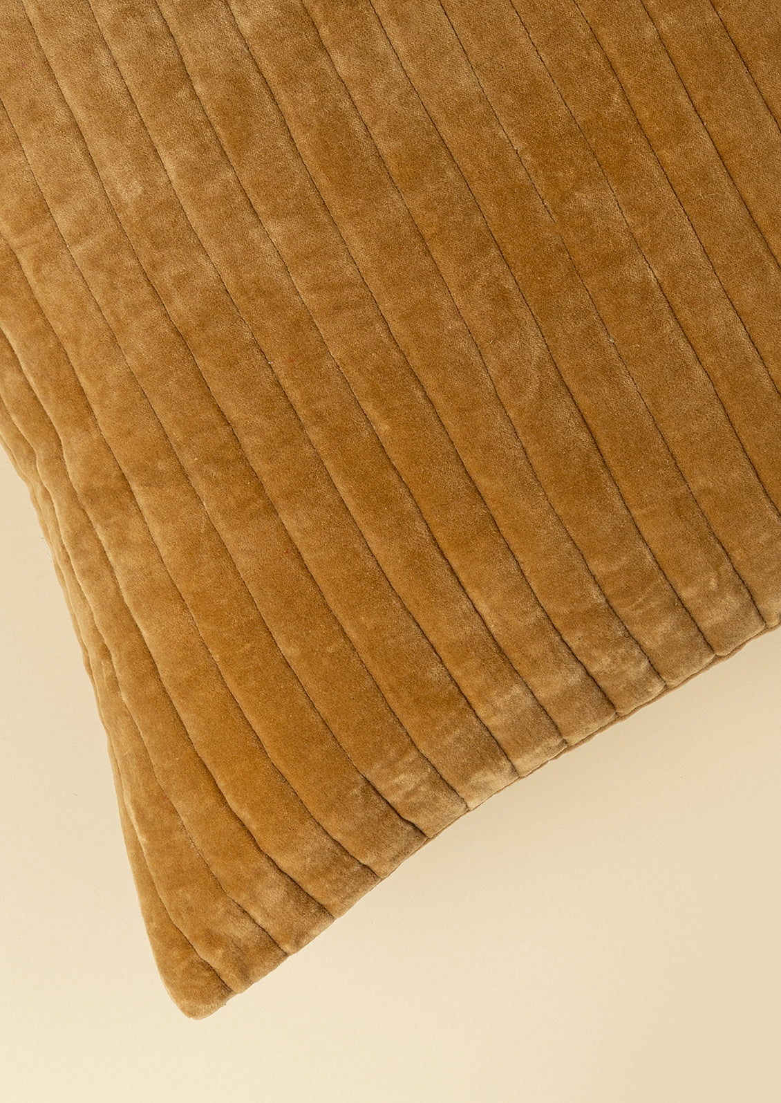 A close-up of a brown pillow showing its vertical ribbed texture and plush velvet-like fabric against a light beige background.