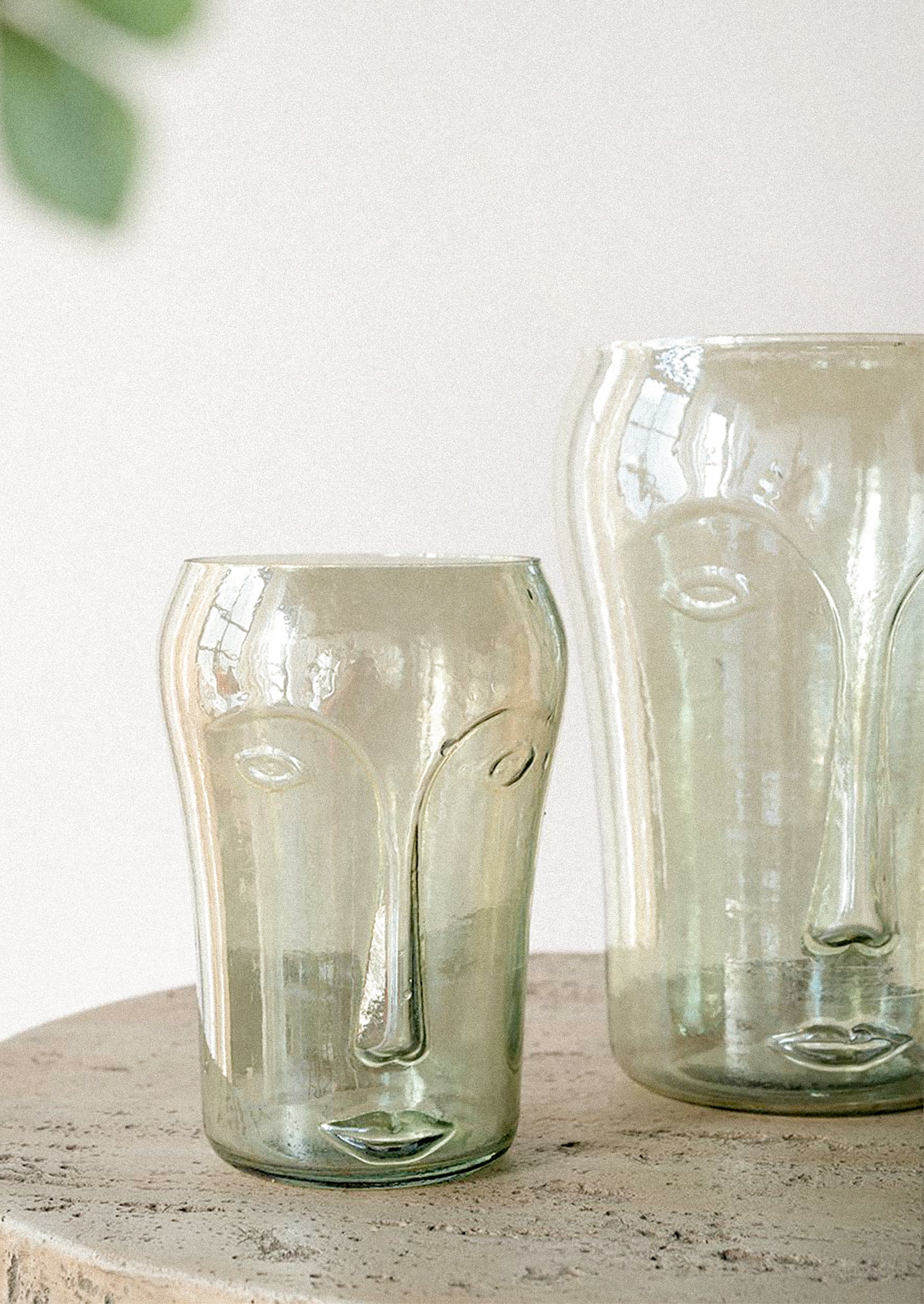 Two translucent smoky green glass vessels with embossed face details.