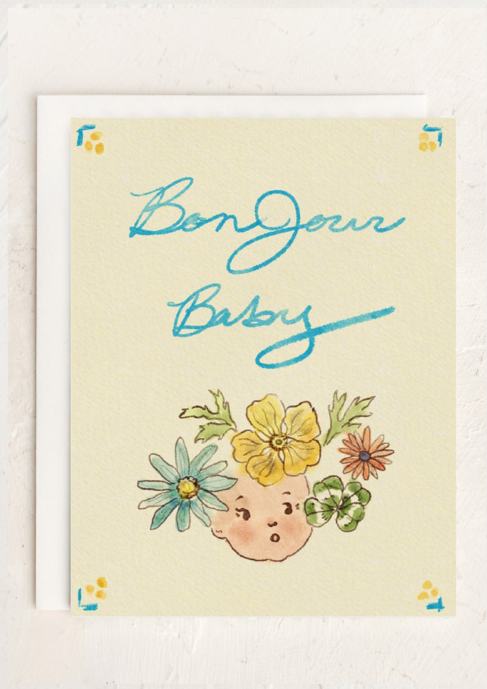 A greeting card with floral baby face illustration reading "Bonjour Baby".