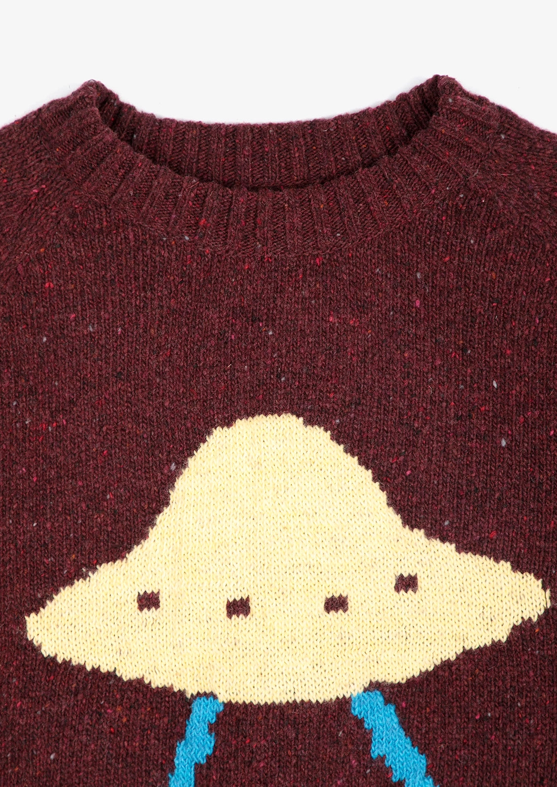 Close-up of a maroon knit sweater featuring a large cream-colored UFO motif with small dark details and light blue legs.
