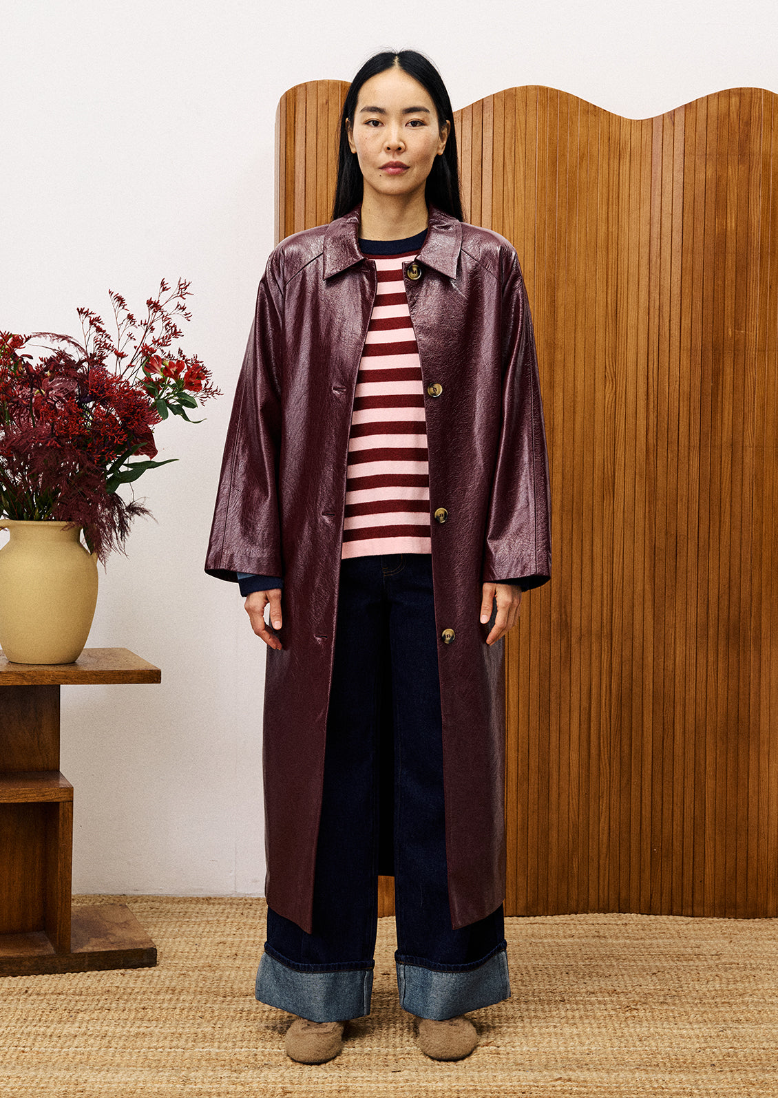 Person wearing a long coat over a striped shirt with a wooden background