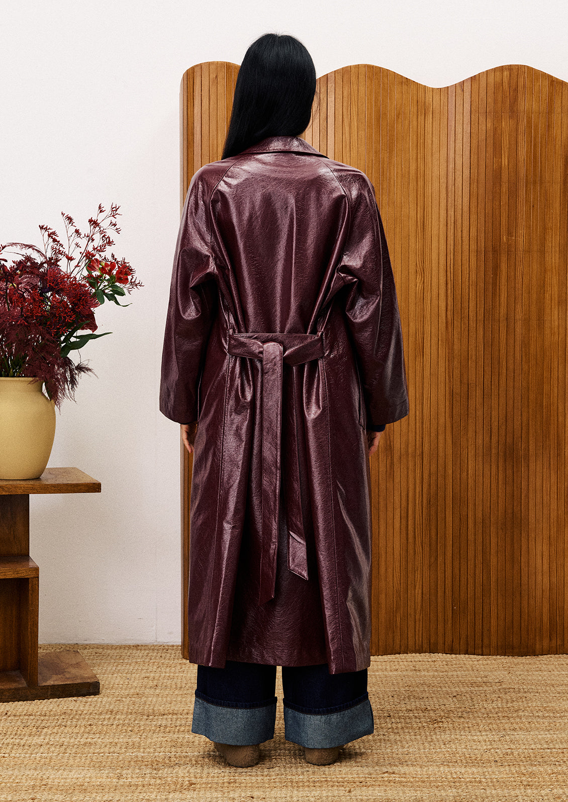 Person wearing a brown satin robe standing in front of a wooden screen with a vase of flowers on a table to their left.