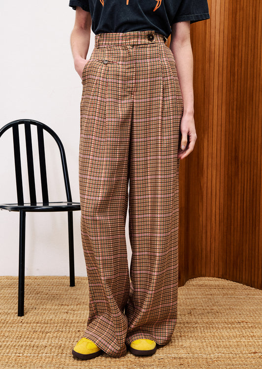 Person wearing brown plaid pants standing against a wooden wall.