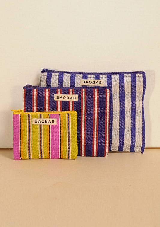 Three striped fabric pouches from BAOBAB, arranged by size against a plain beige background. The smallest pouch is yellow, pink, and orange striped; the middle pouch is navy, red, and white striped; the largest pouch is blue and white striped.