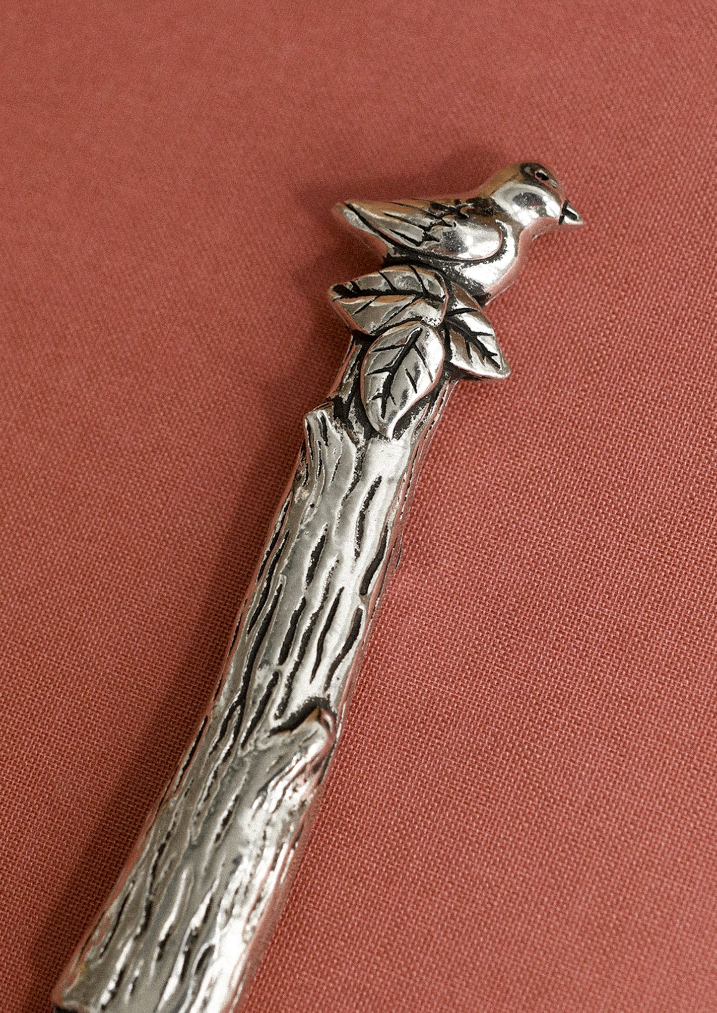 Silver spoon with bird and branch design on a red background