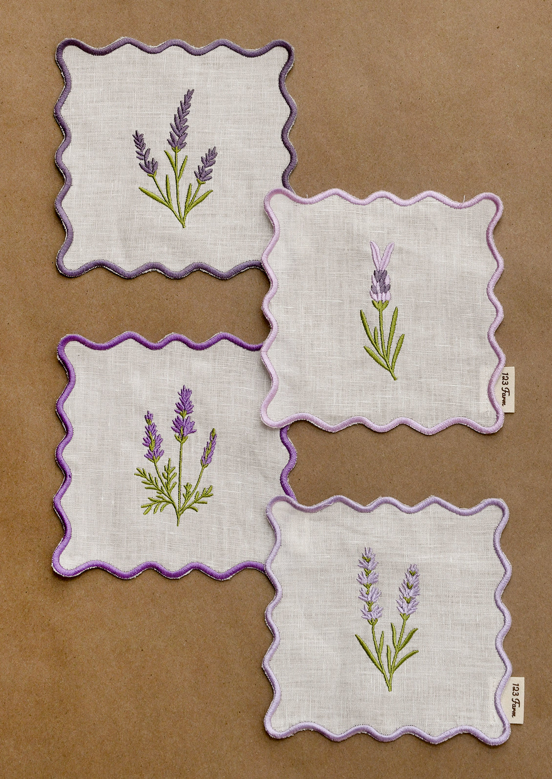 A set of four square cocktail napkins with scalloped purple edges and lavender sprig embroidery.