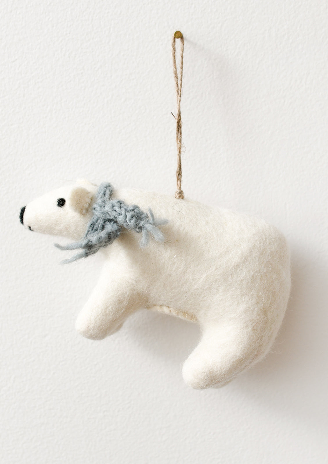 A white felt polar bear Christmas ornament with a knitted blue-gray scarf and a brown jute hanging loop.