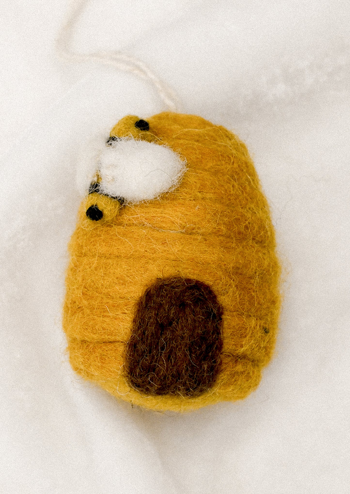 A small felted wool ornament depicting a beehive.