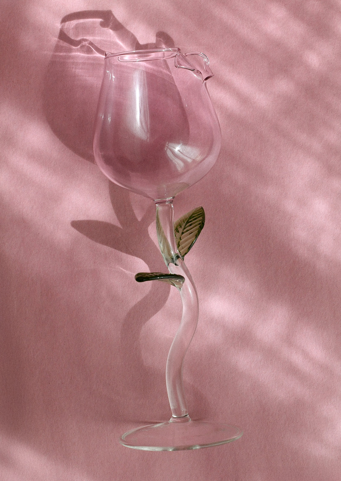 A wine glass in the shape of a pink rosebud, with green leaf detail on stem.