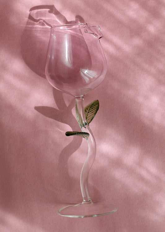 A wine glass in the shape of a pink rosebud, with green leaf detail on stem.