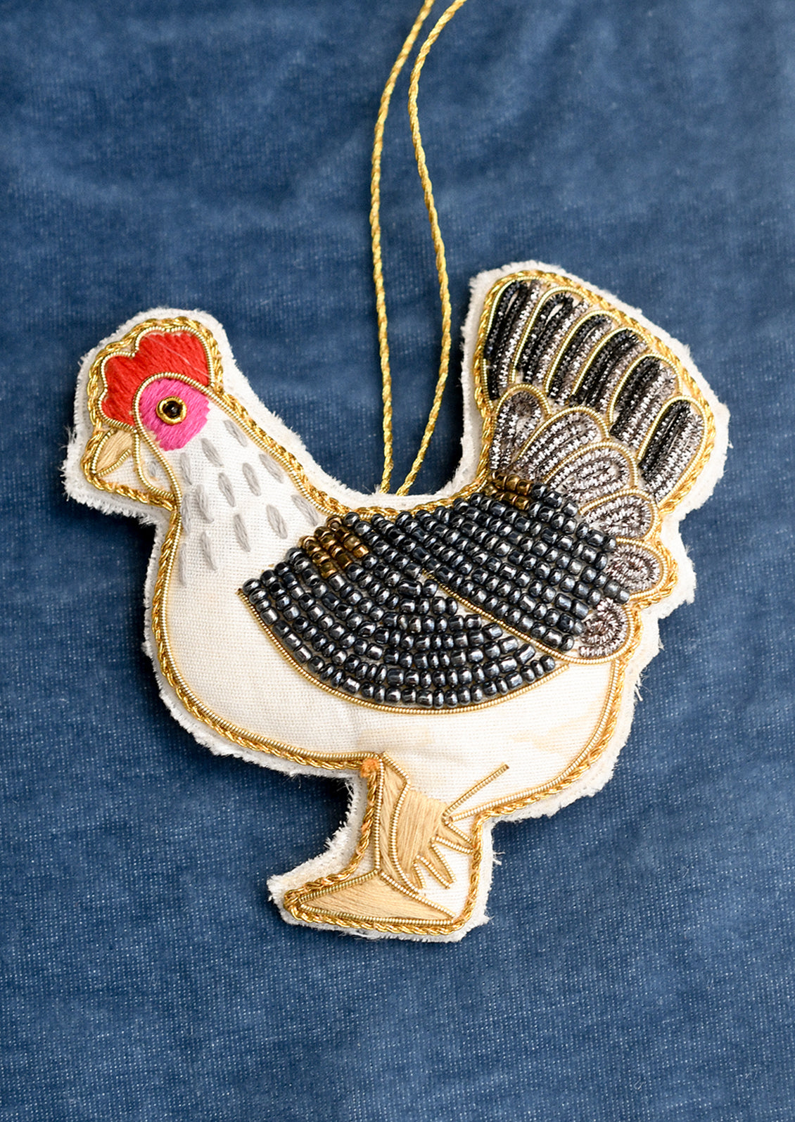 A fabric ornament depicting a chicken, with beading and embroidery details.