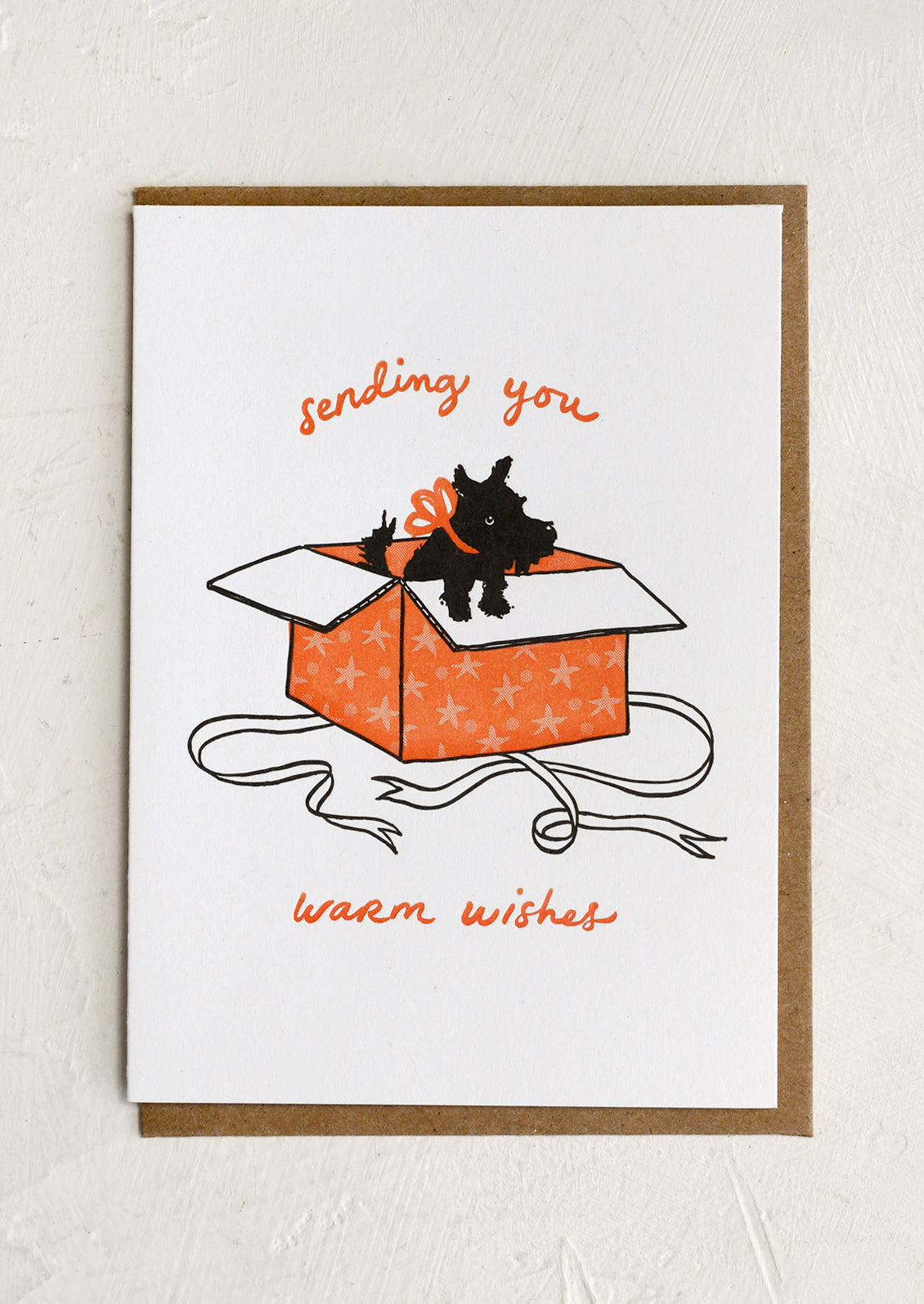 A greeting card with image of black Scottie dog jumping out of gift box, text reads "Sending you warm wishes".