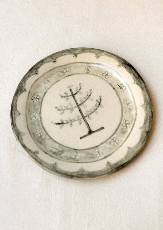 A cream ceramic plate with illustrated tree and flowers in dark grey.