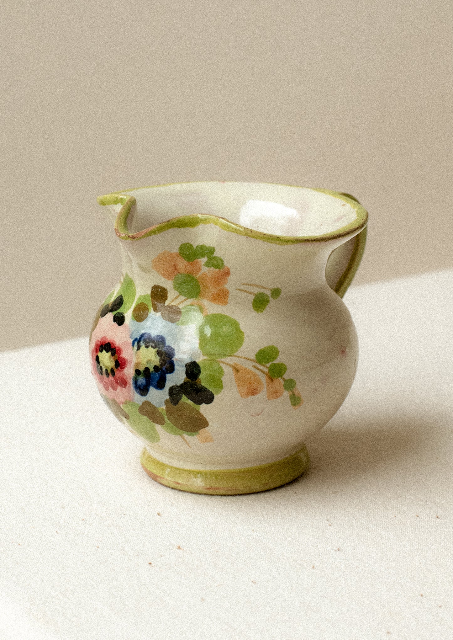 A small ceramic pitcher with painted floral design and green border.