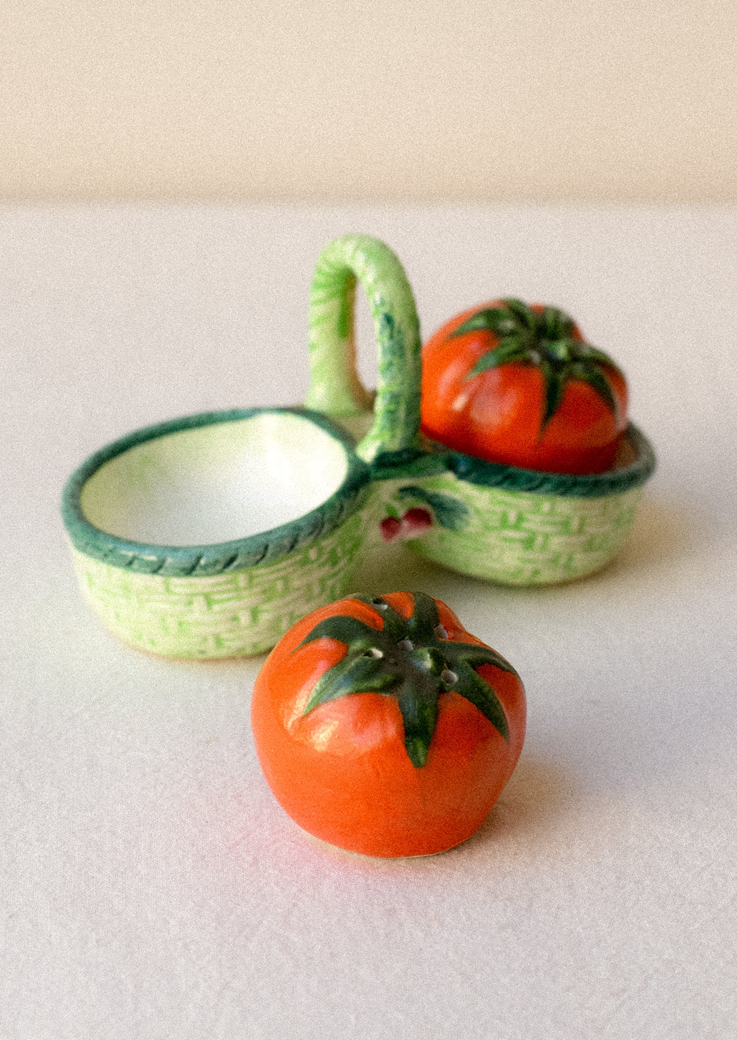 Salt and pepper shakers shaped like tomatoes in a decorative green basket.