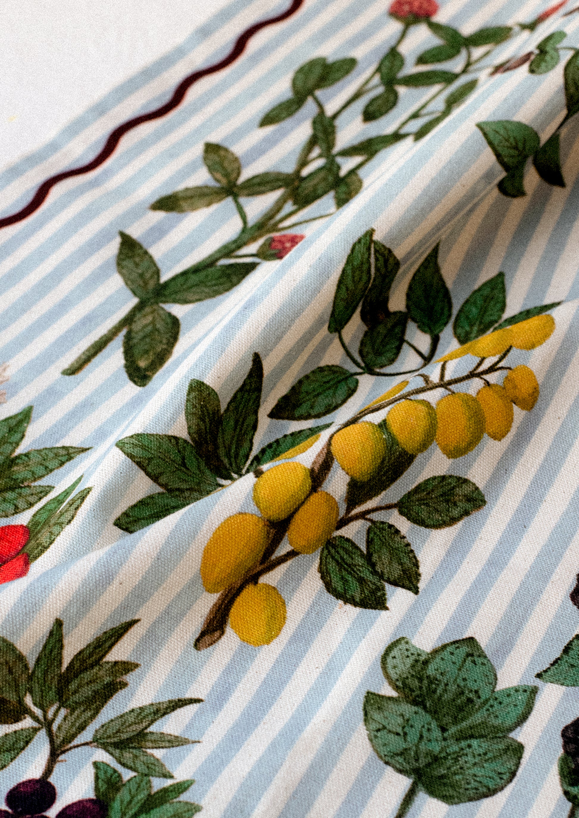 Close-up of an organic cotton tea towel with light blue stripes and a floral and fruit watercolor illustration.