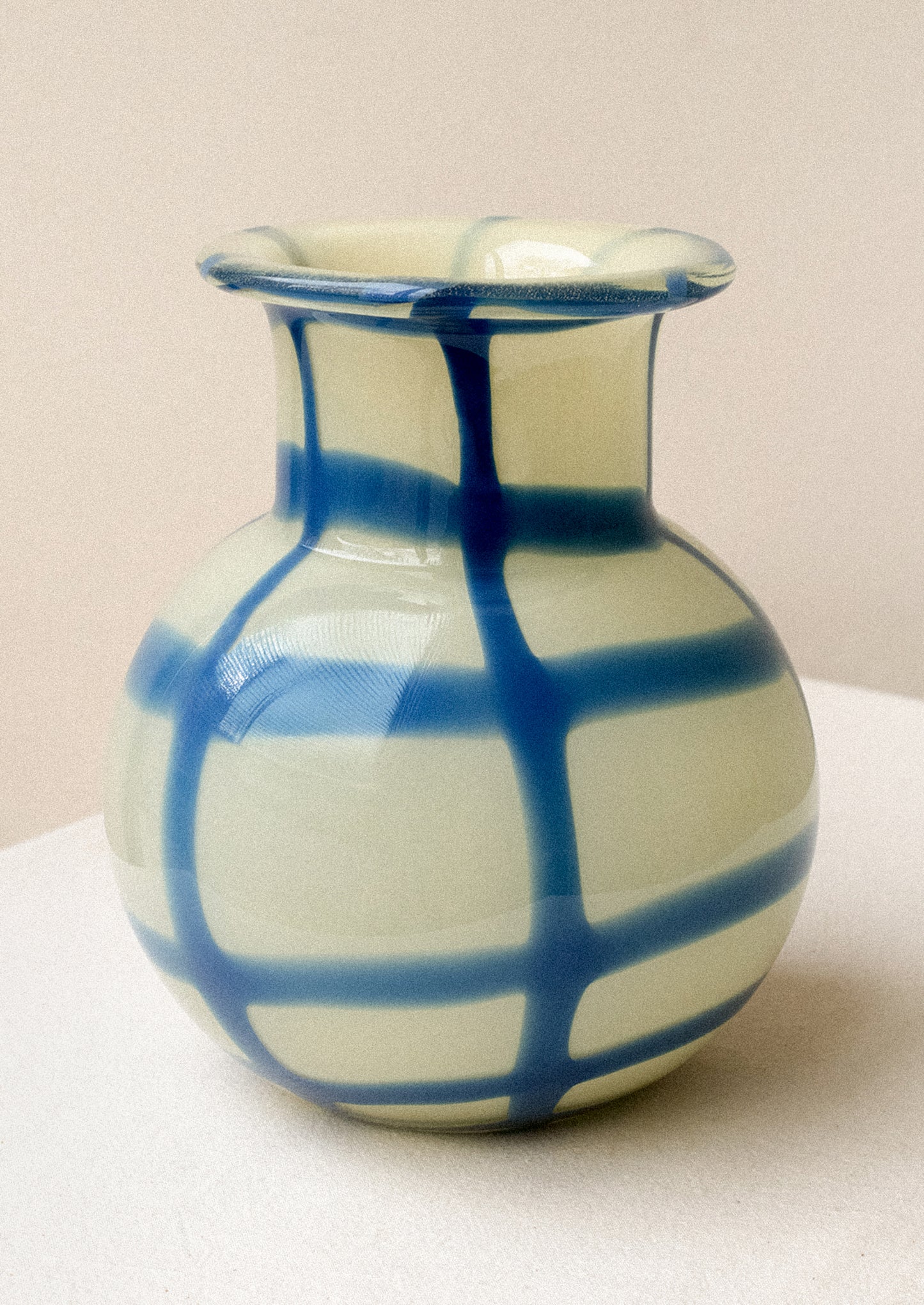 A glass vase with round shape, in yellow with painted blue gingham pattern.