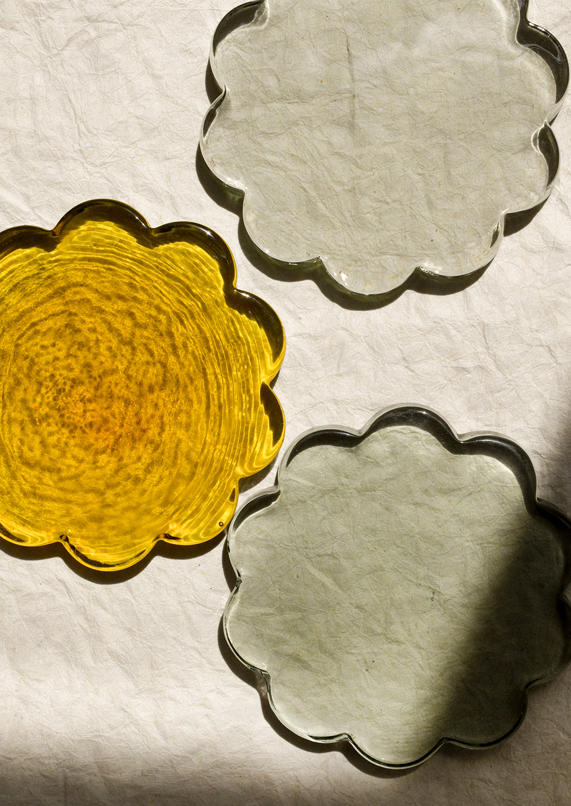 Three floral-shaped glass coasters in yellow, gray, and green.
