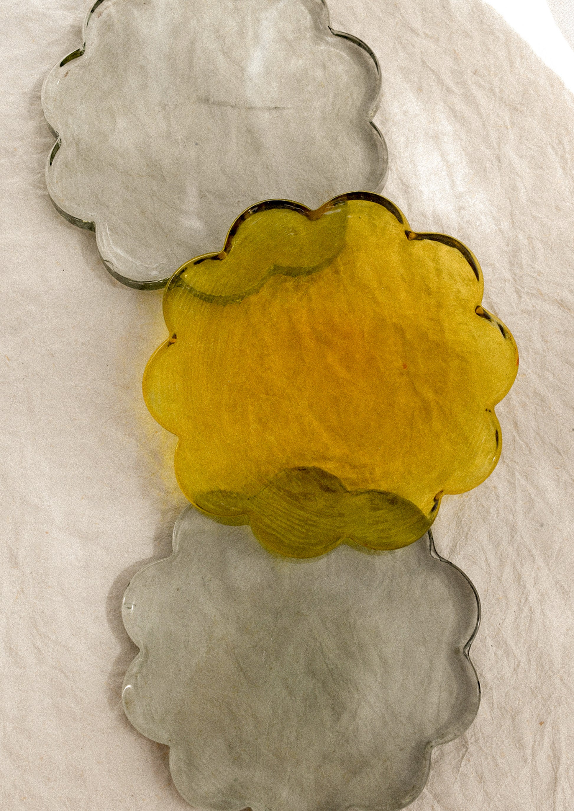 Three floral-shaped glass coasters in yellow, gray, and green.