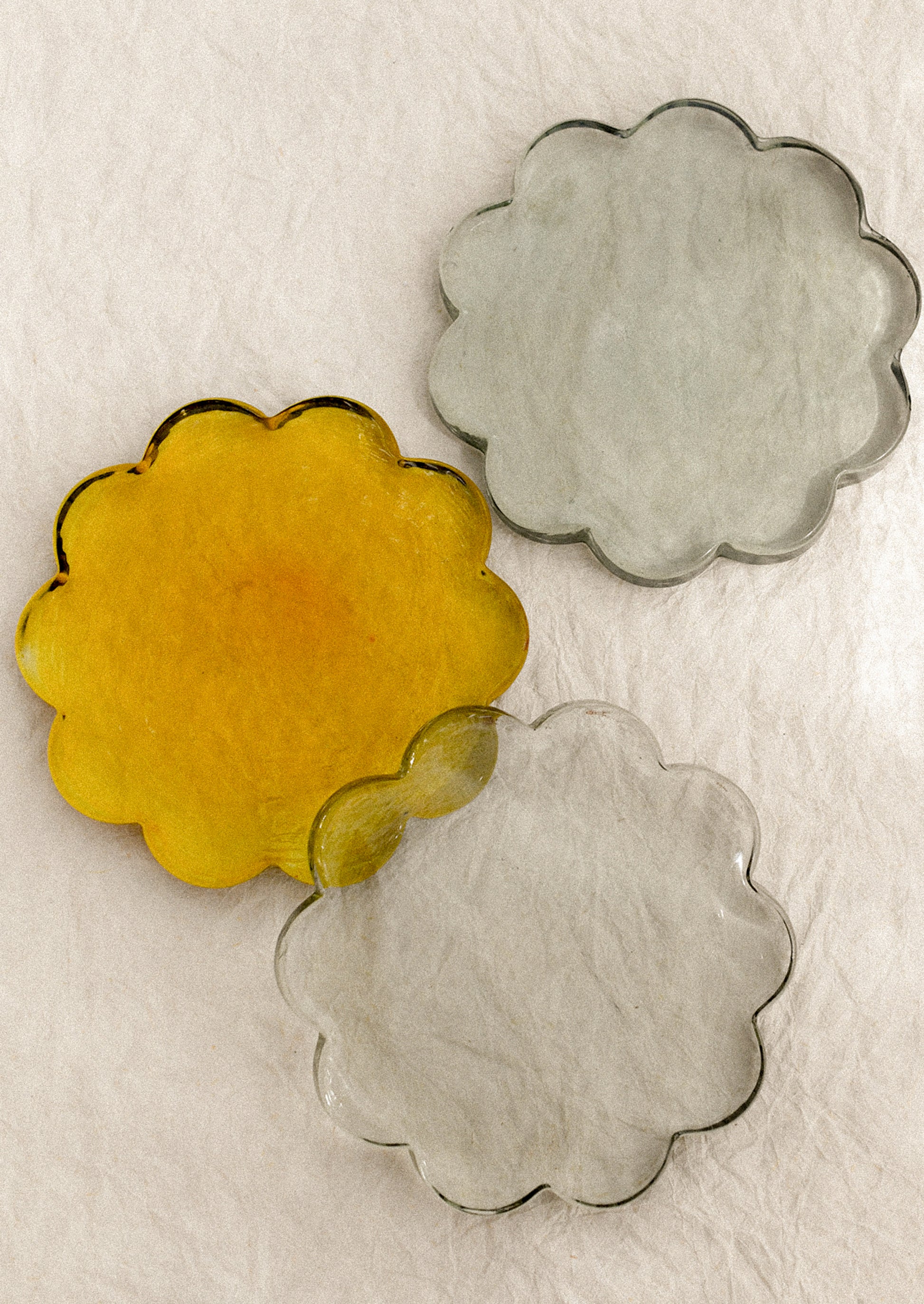 Three floral-shaped glass coasters in yellow, gray, and green.