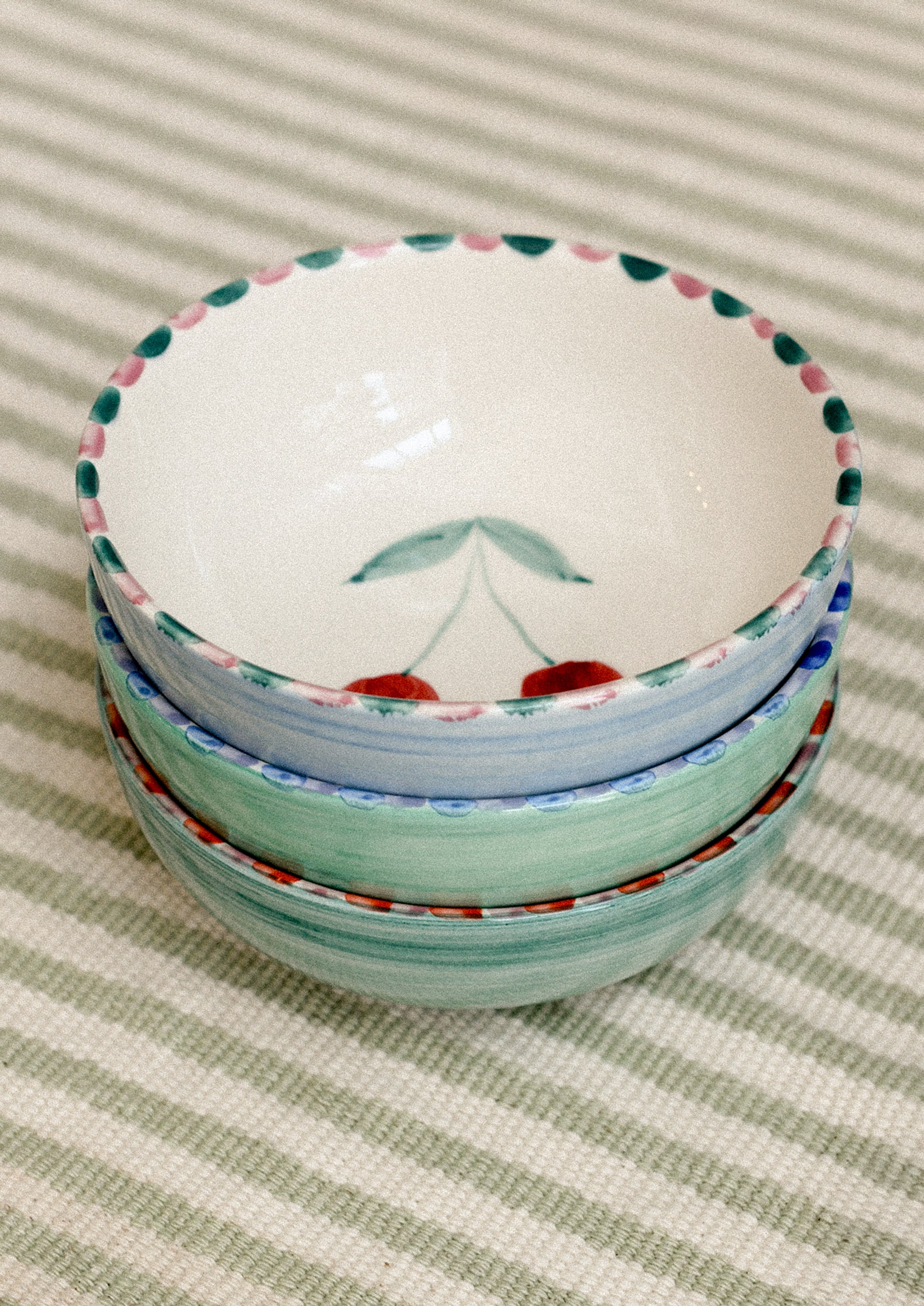 Stack of ceramic bowls with colorful rims on a striped fabric background.