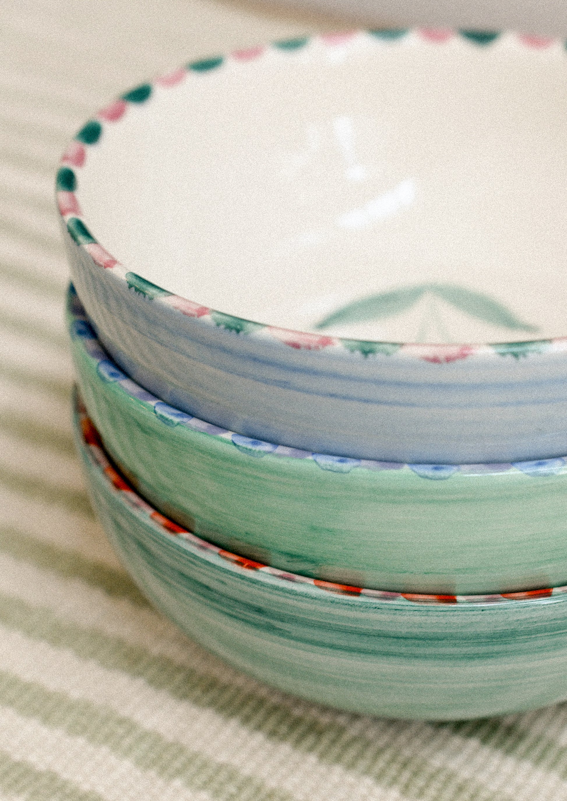 Stack of ceramic bowls with colorful rims on a striped fabric background.