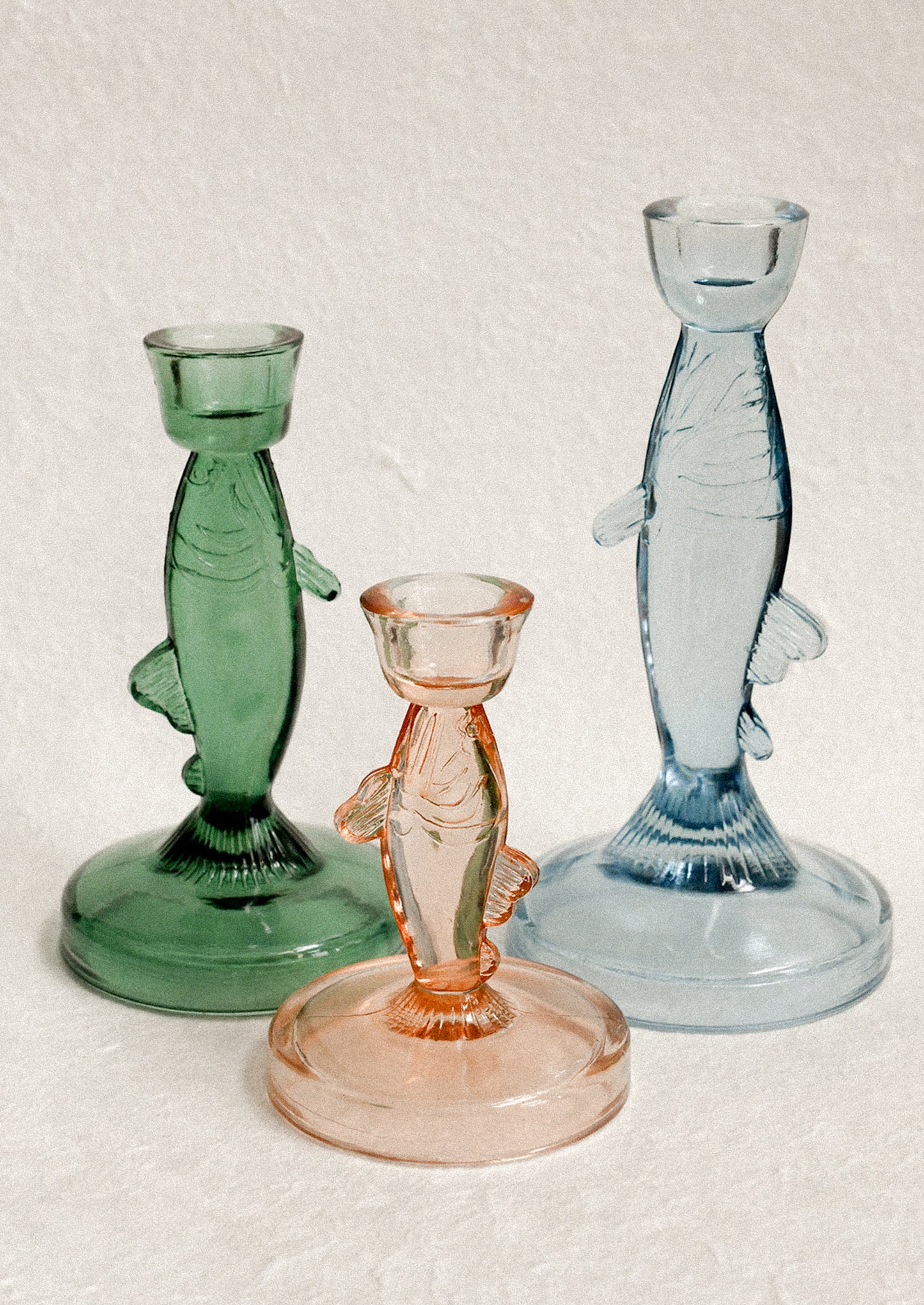 Three fish-shaped glass candle holders in green, pink, and blue.
