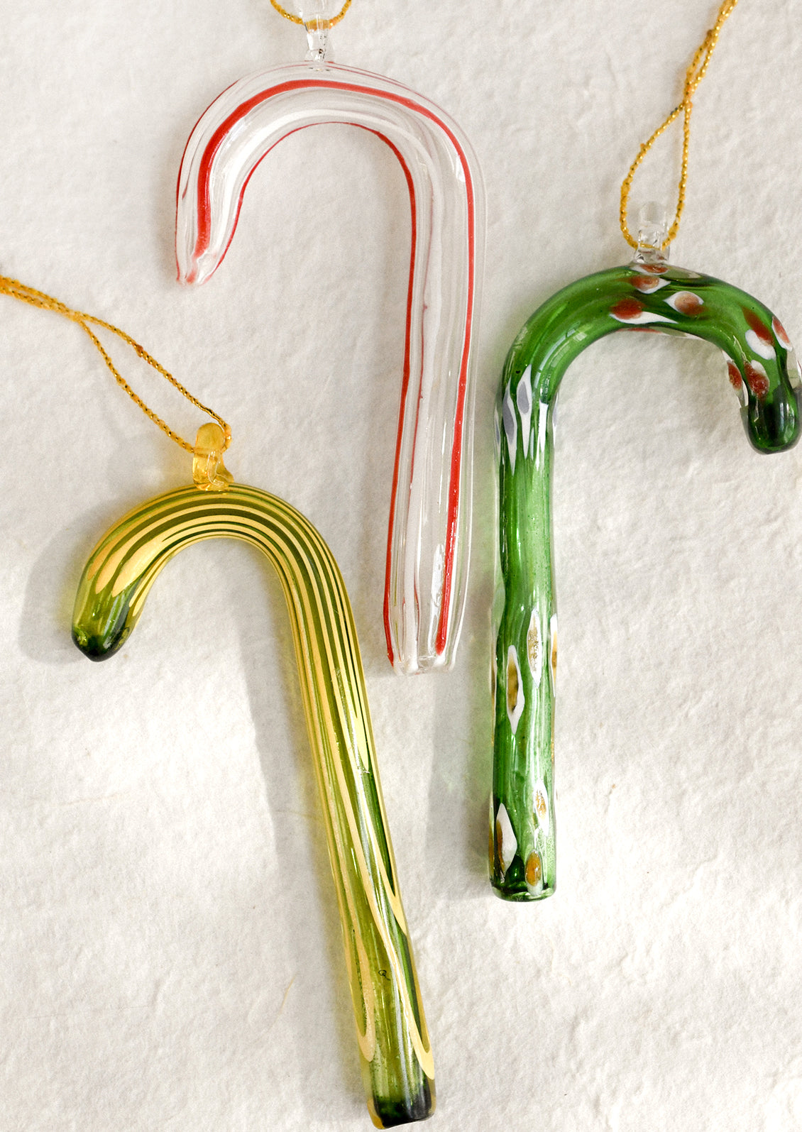 Three glass candy cane ornaments on a textured white background