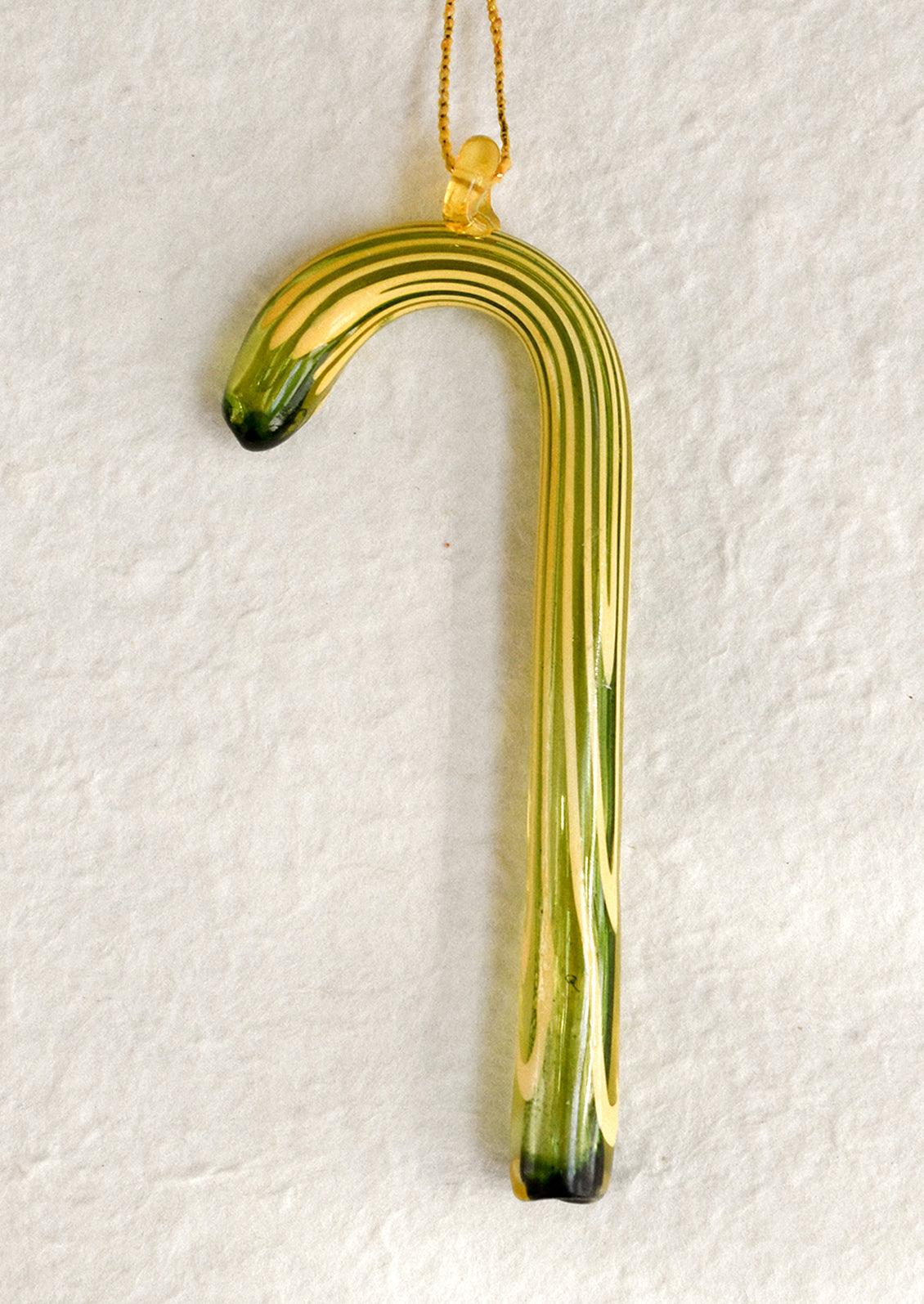 Decorative glass cane ornament with green and yellow pattern on a white background