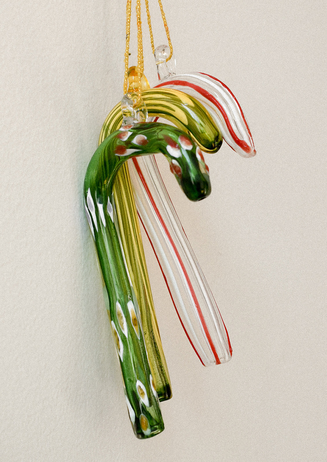 Glass candy canes in green, gold, and red on a beige background
