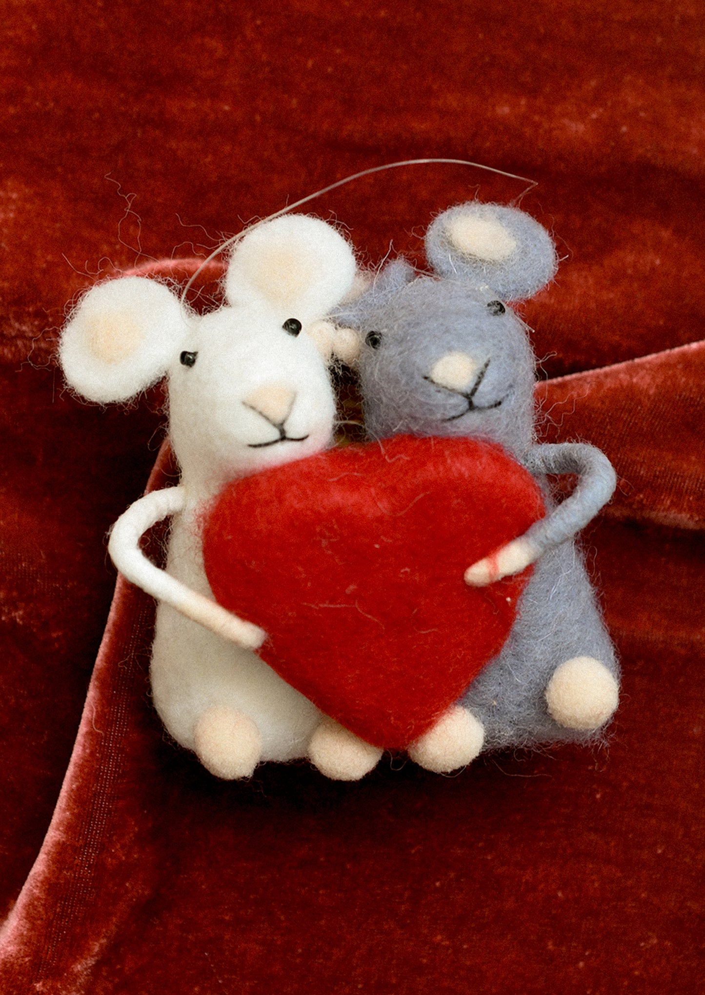 A felted holiday ornament of a white mouse and a gray mouse holding a red heart.