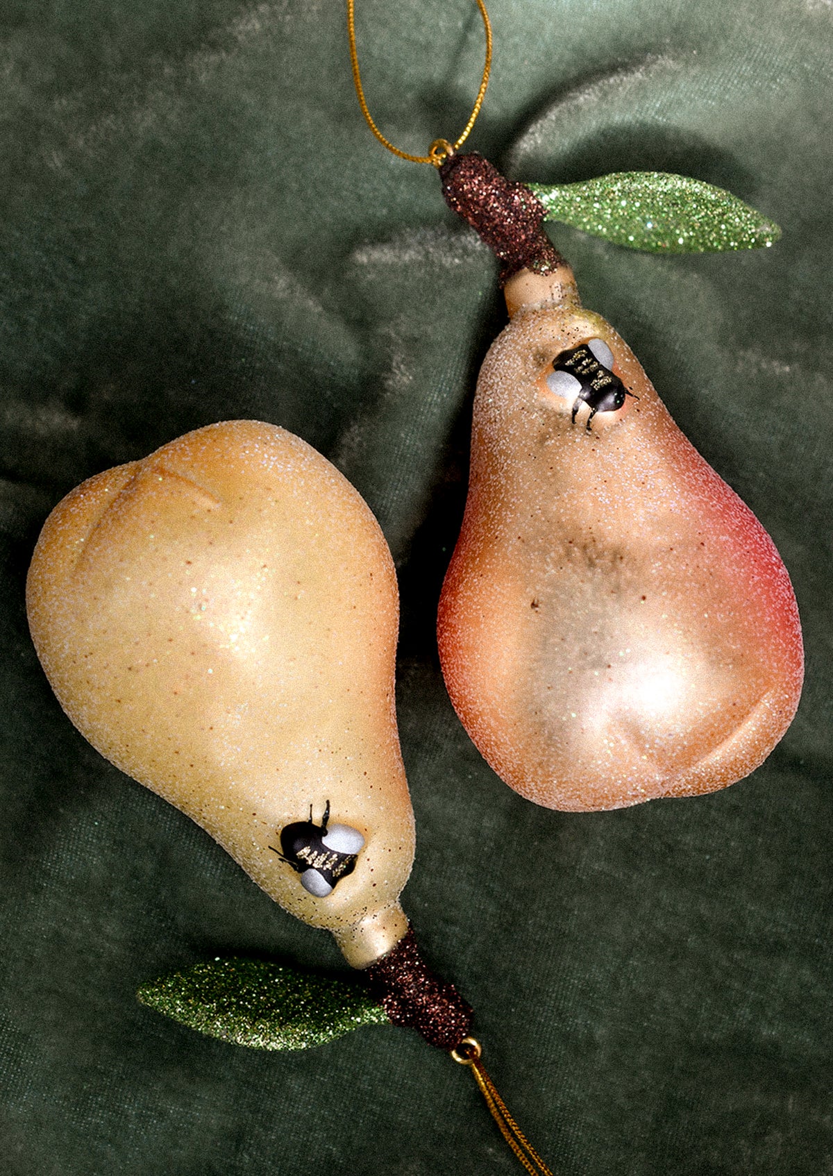 Two pear-shaped ornaments on a green fabric background