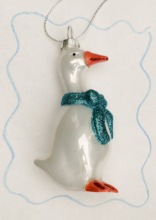 A glass ornament of a white goose wearing blue bow ribbon around its neck.