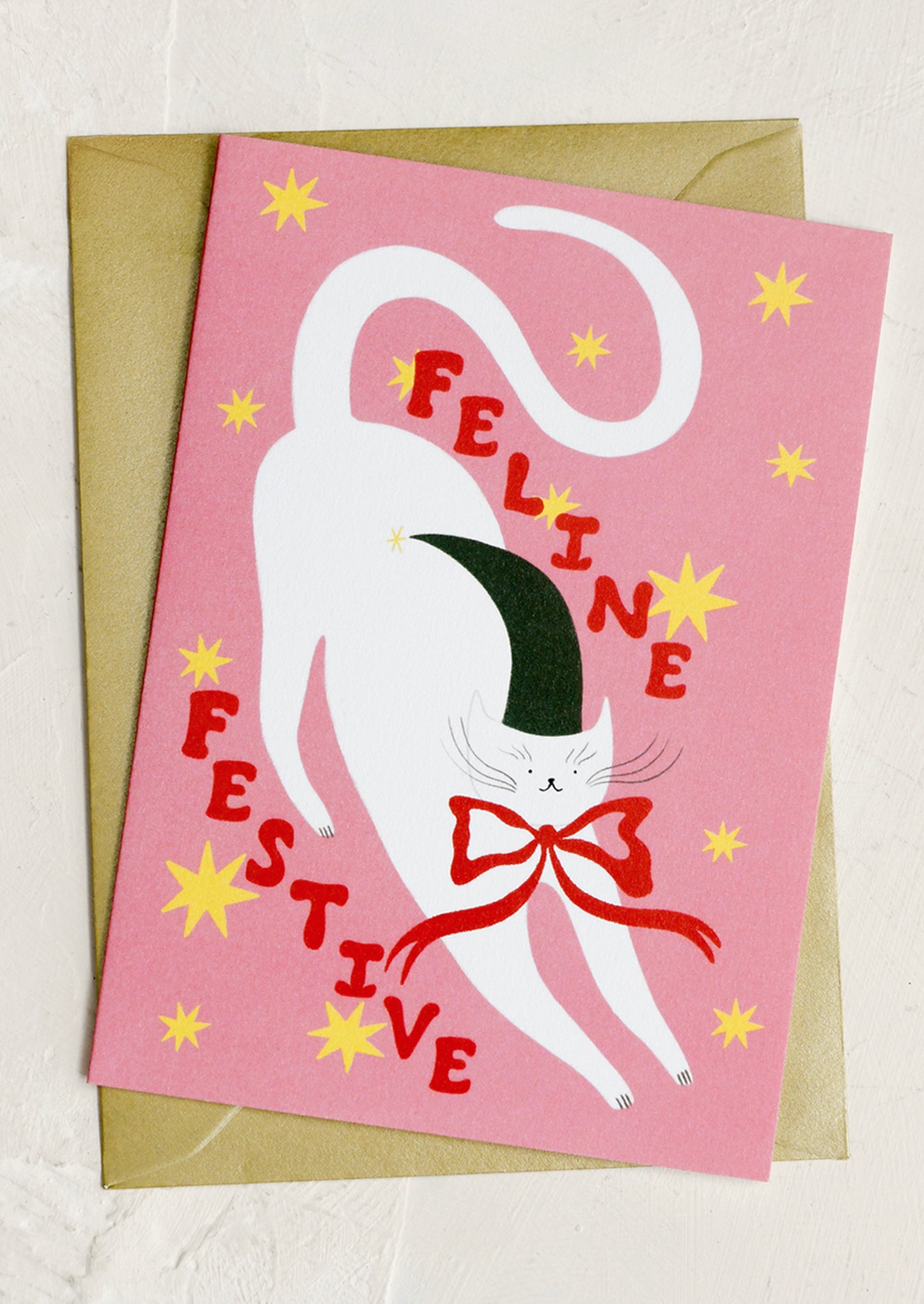 Greeting card with a cat illustration and 'Feline Festive' text on a pink background.