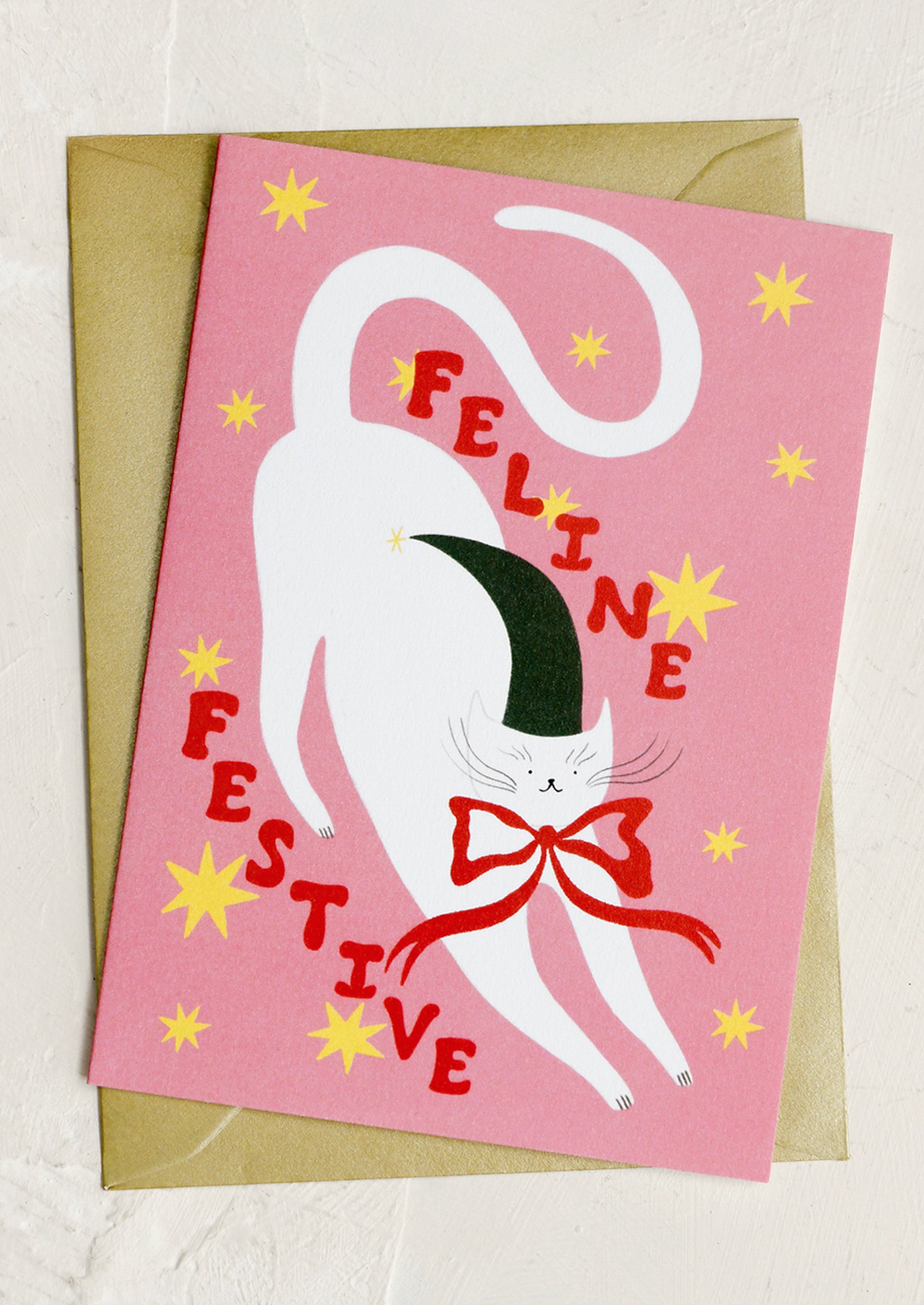 Greeting card with a cat illustration and 'Feline Festive' text on a pink background.
