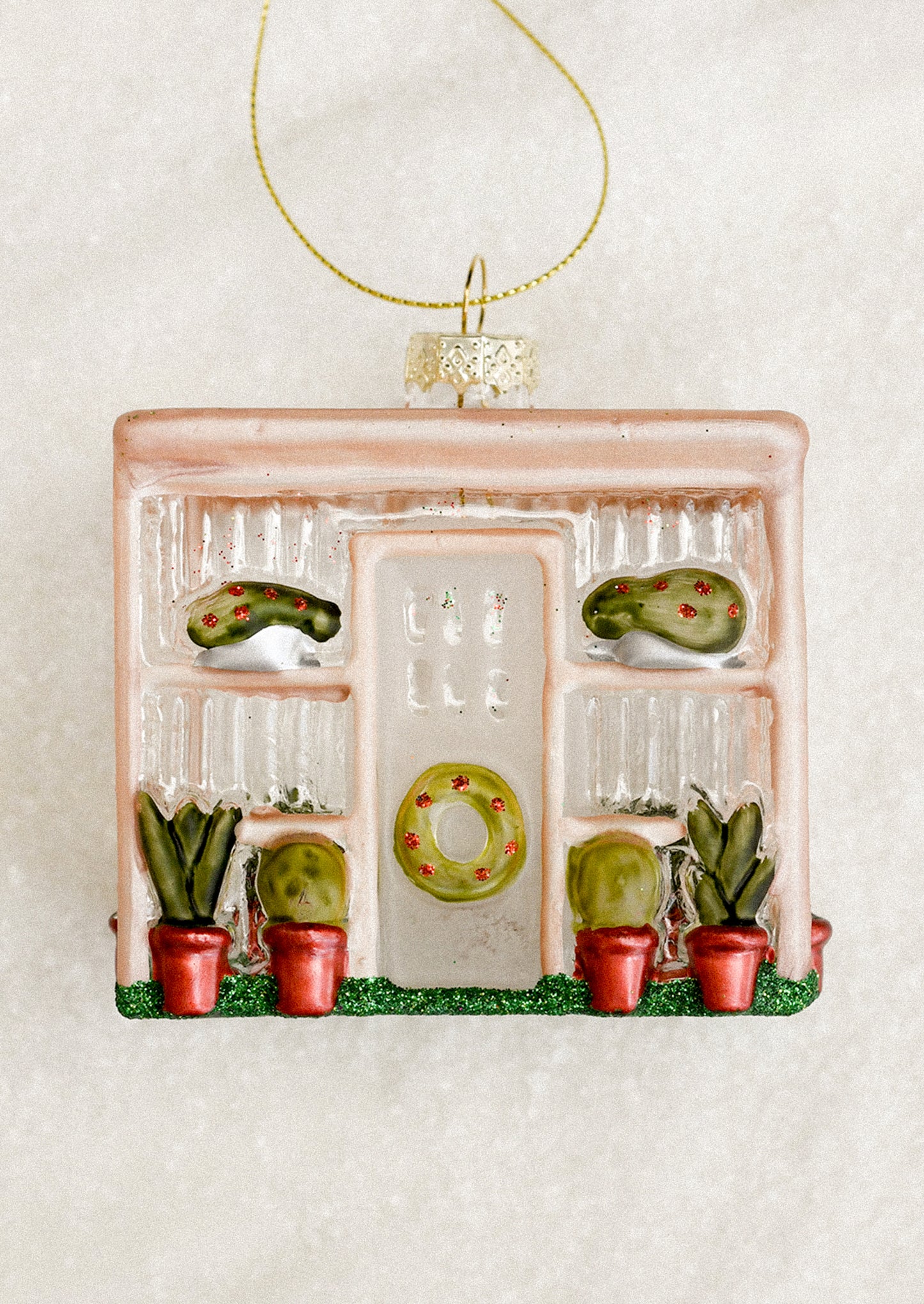 A decorative glass ornament depicting a greenhouse, with wreath decorations.