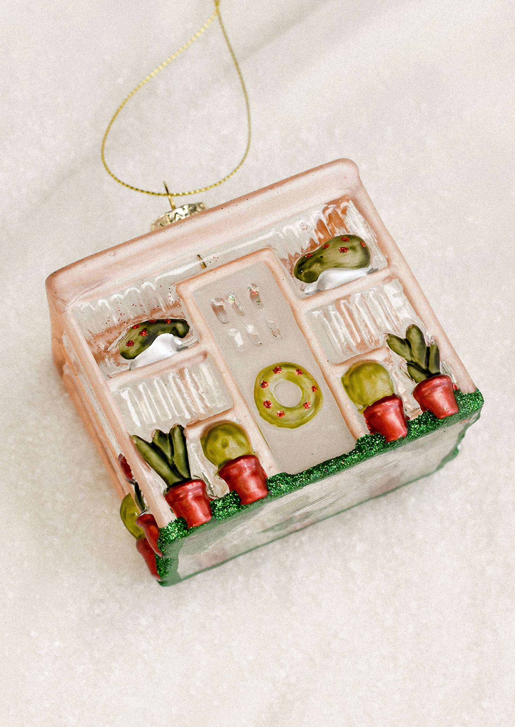 A decorative glass ornament depicting a greenhouse, with wreath decorations.
