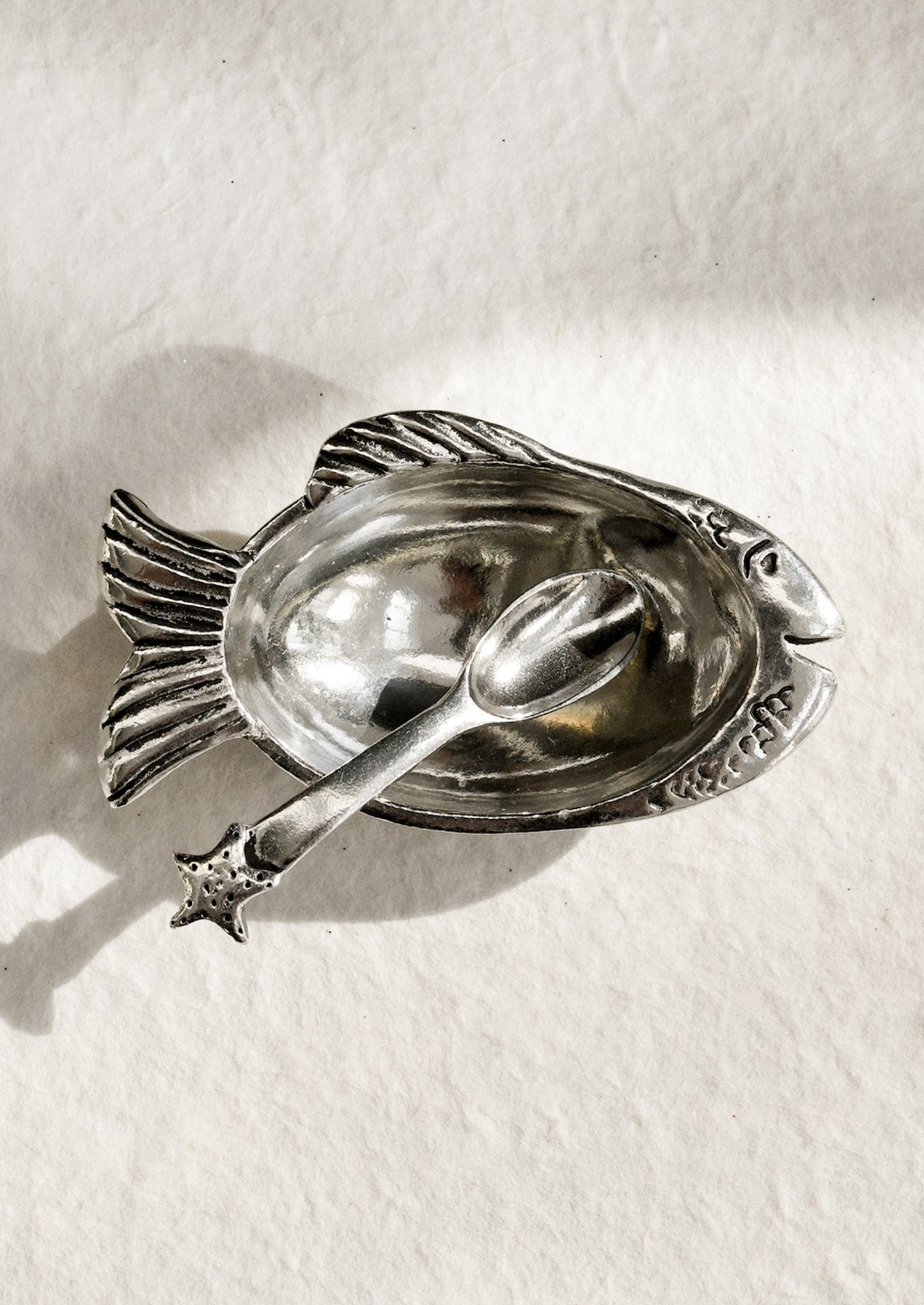 Silver fish-shaped dish with spoon on a white background
