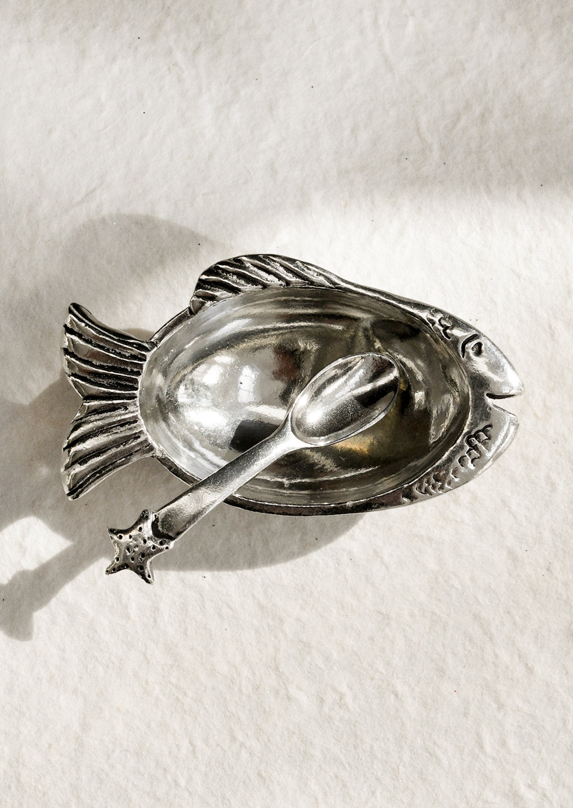 Silver fish-shaped dish with spoon on a white background