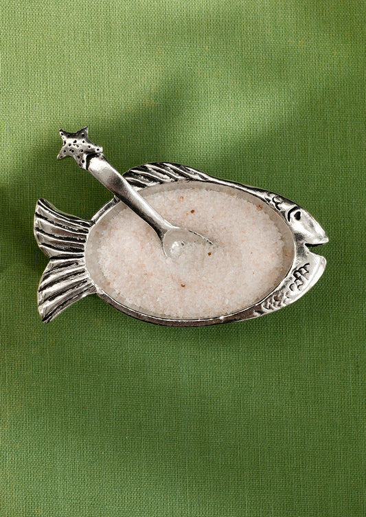 Decorative fish-shaped salt cellar with a spoon on a green background