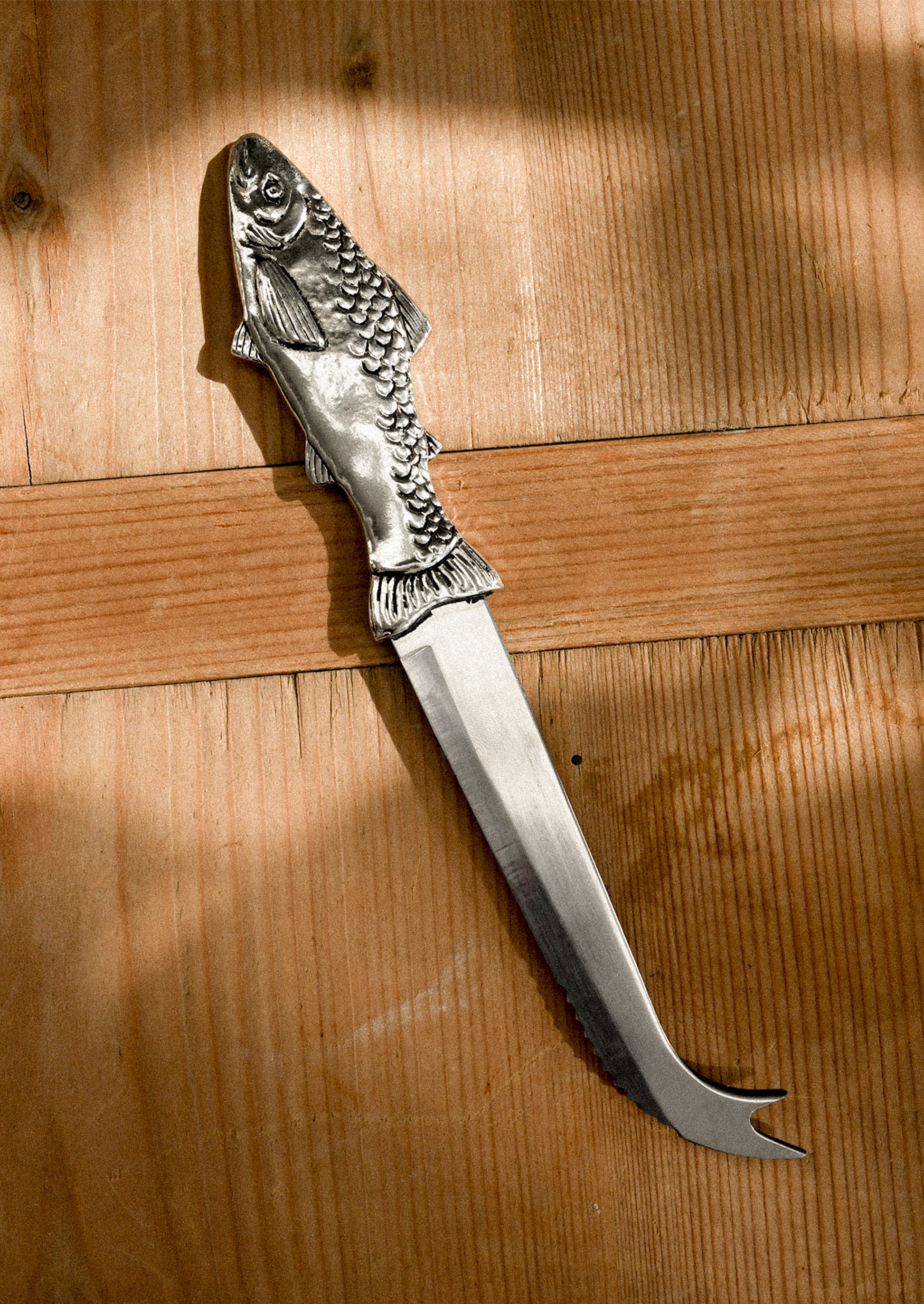 A pewter serrated cheese knife with pronged end, and fish-shaped handle.