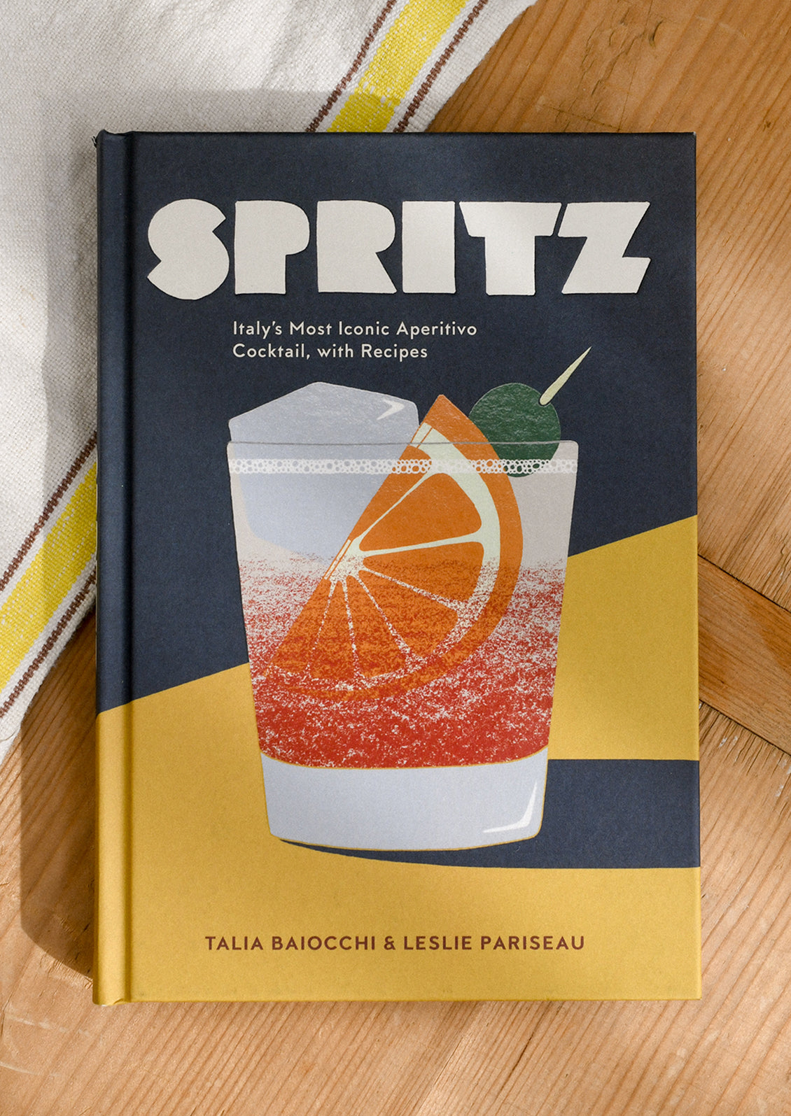 Book titled 'Spritz' on a wooden surface with a striped fabric background