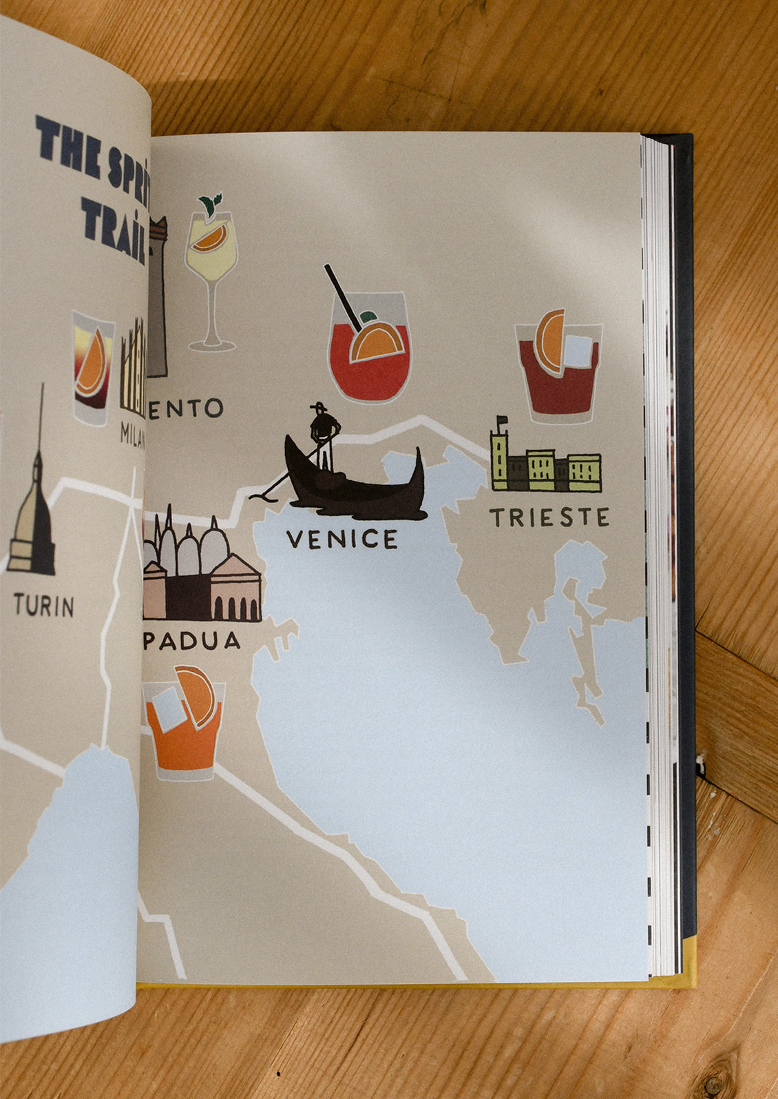 Open book showing a map of Italy with illustrations of Venice and Trieste on a wooden surface.