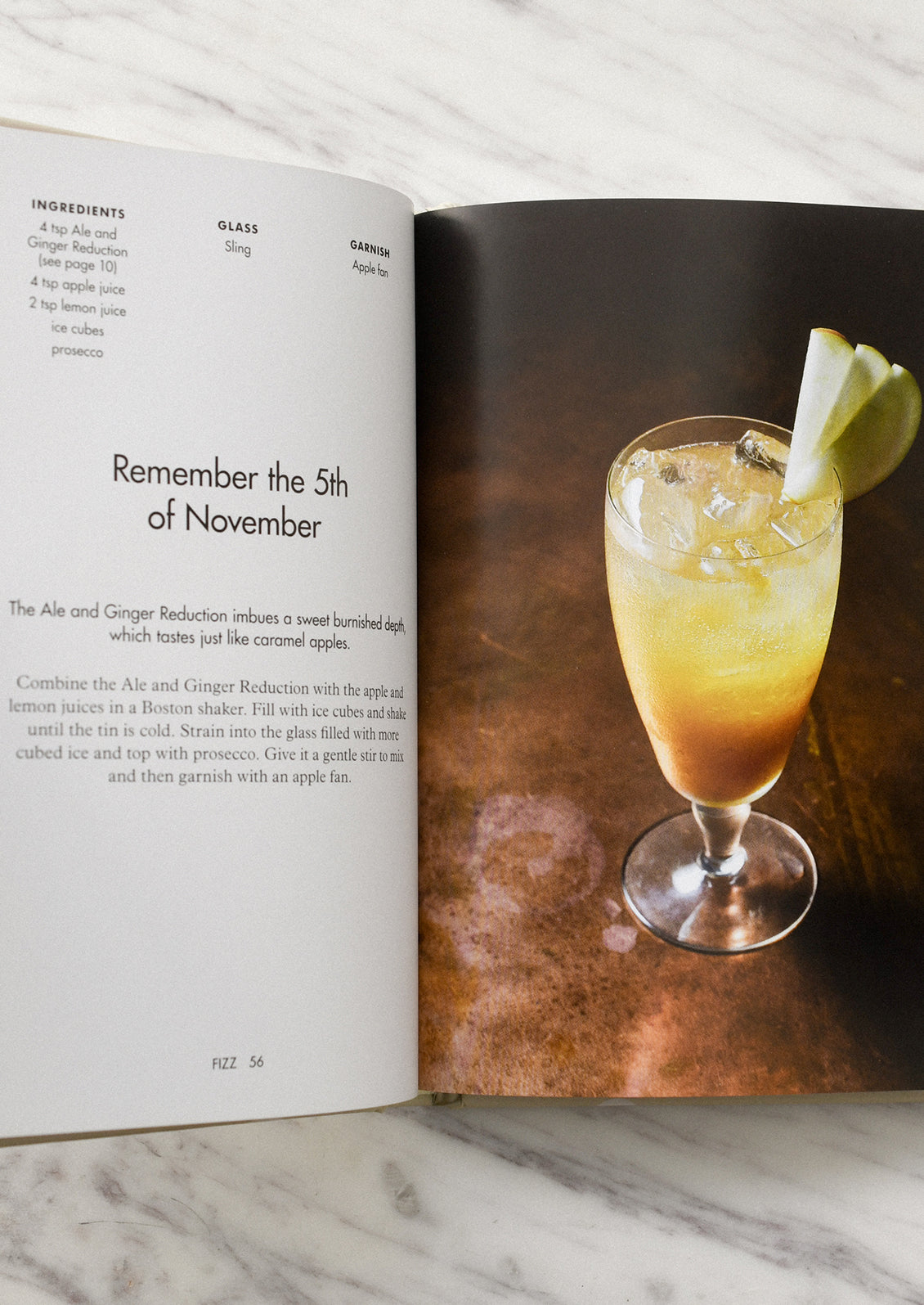 Open book with a cocktail recipe and a glass of cocktail on a marble surface