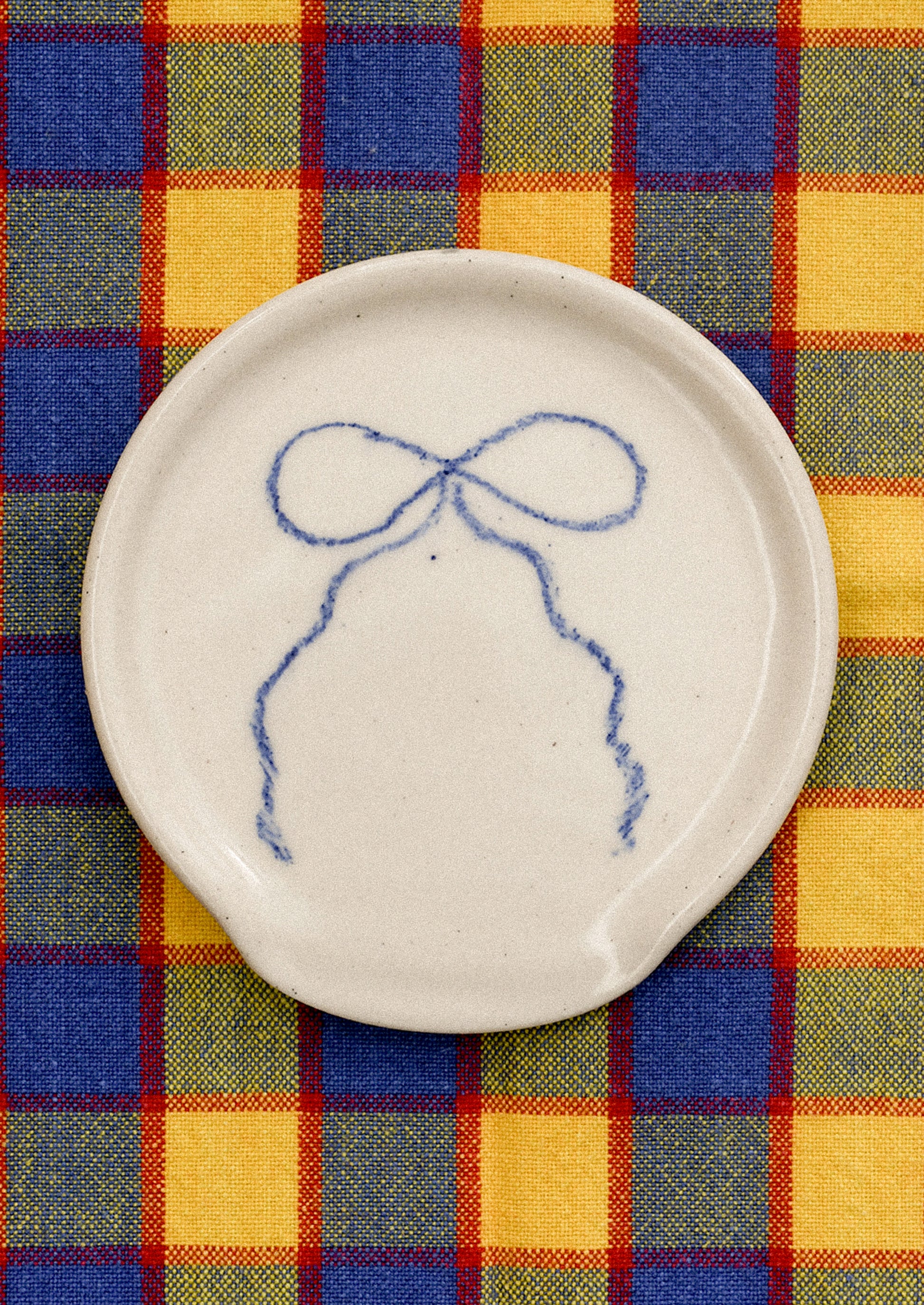 White ceramic plate with blue bow design on a colorful plaid fabric background