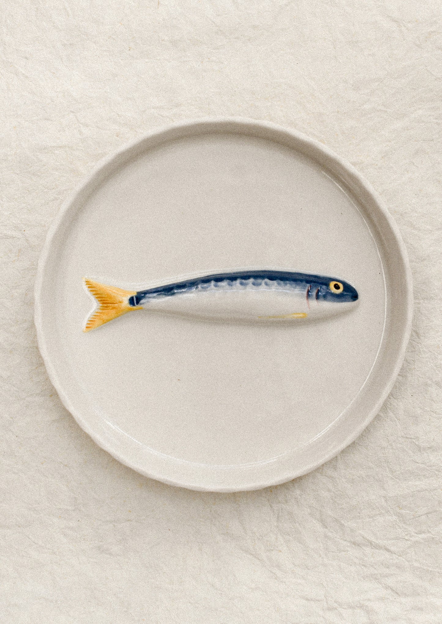 Ceramic fish-shaped object on a round plate with a plain background