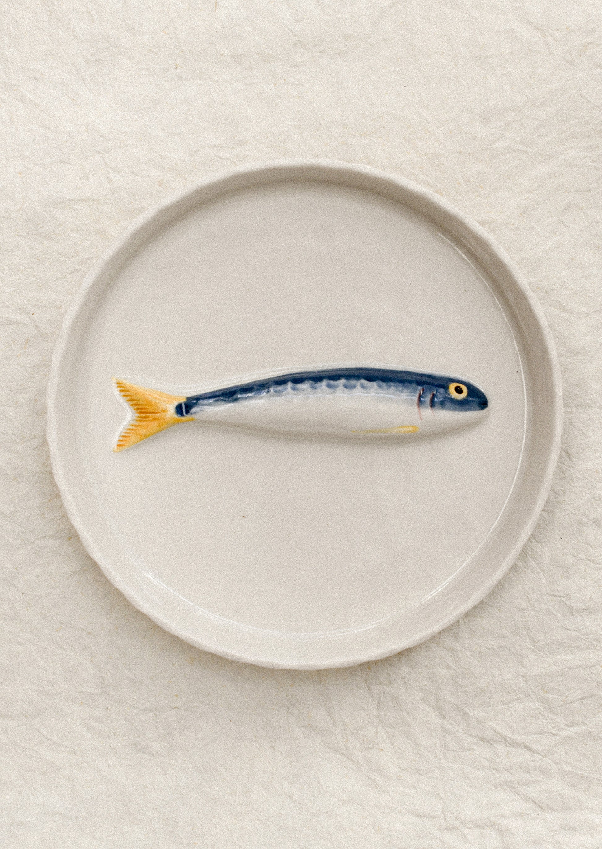 Ceramic fish-shaped object on a round plate with a plain background