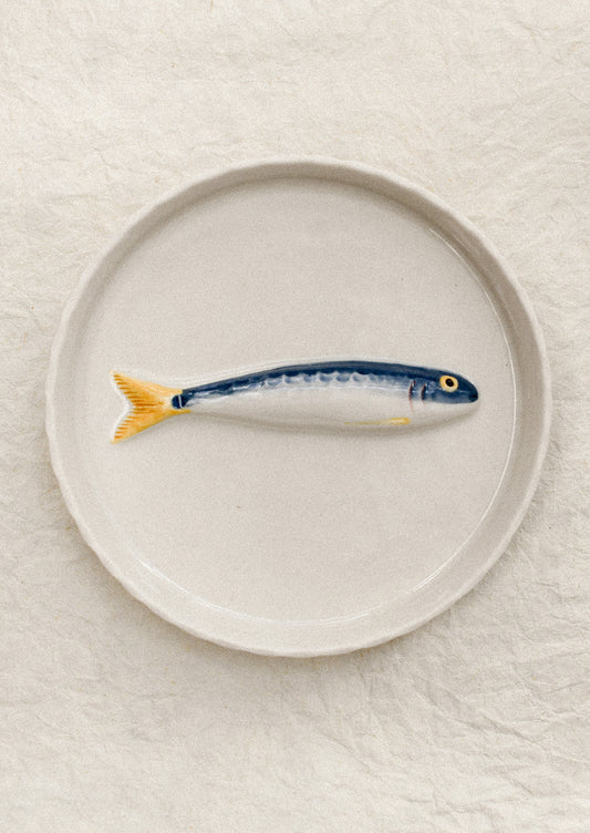 Ceramic fish-shaped object on a round plate with a plain background